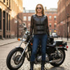 Woman wearing the black leather motorcycle vest beside a motorcycle, front view.
