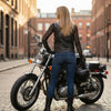Woman wearing the black leather motorcycle vest beside a motorcycle, back view.